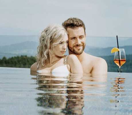 blonde Frau und Mann mit Bart stehen im Infinitypool ndes Wellnesshotel Zum Bräu mit einem Glas Aperol