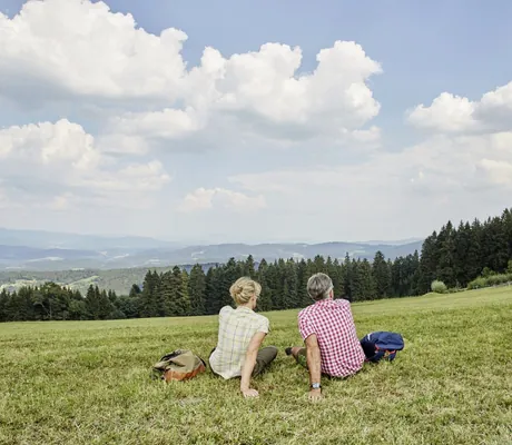 Paar in Karohemden sitzt auf der Wiese des Wellnesshotel Zum Bräu und schaut in die Ferne