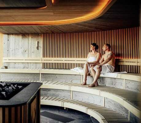 Paar sitzt in der rund geformten Sauna des Wellnesshotel Zum Bräu unter roter Deckenleuchte