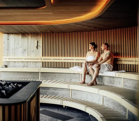 Paar sitzt in der rund geformten Sauna des Wellnesshotel Zum Bräu unter roter Deckenleuchte