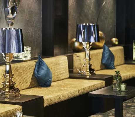 mit goldenem Stoff bezogene Sitzpolster und verschnörkelte Stehlampen in der Lounge des Wellnesshotel Zum Bräu