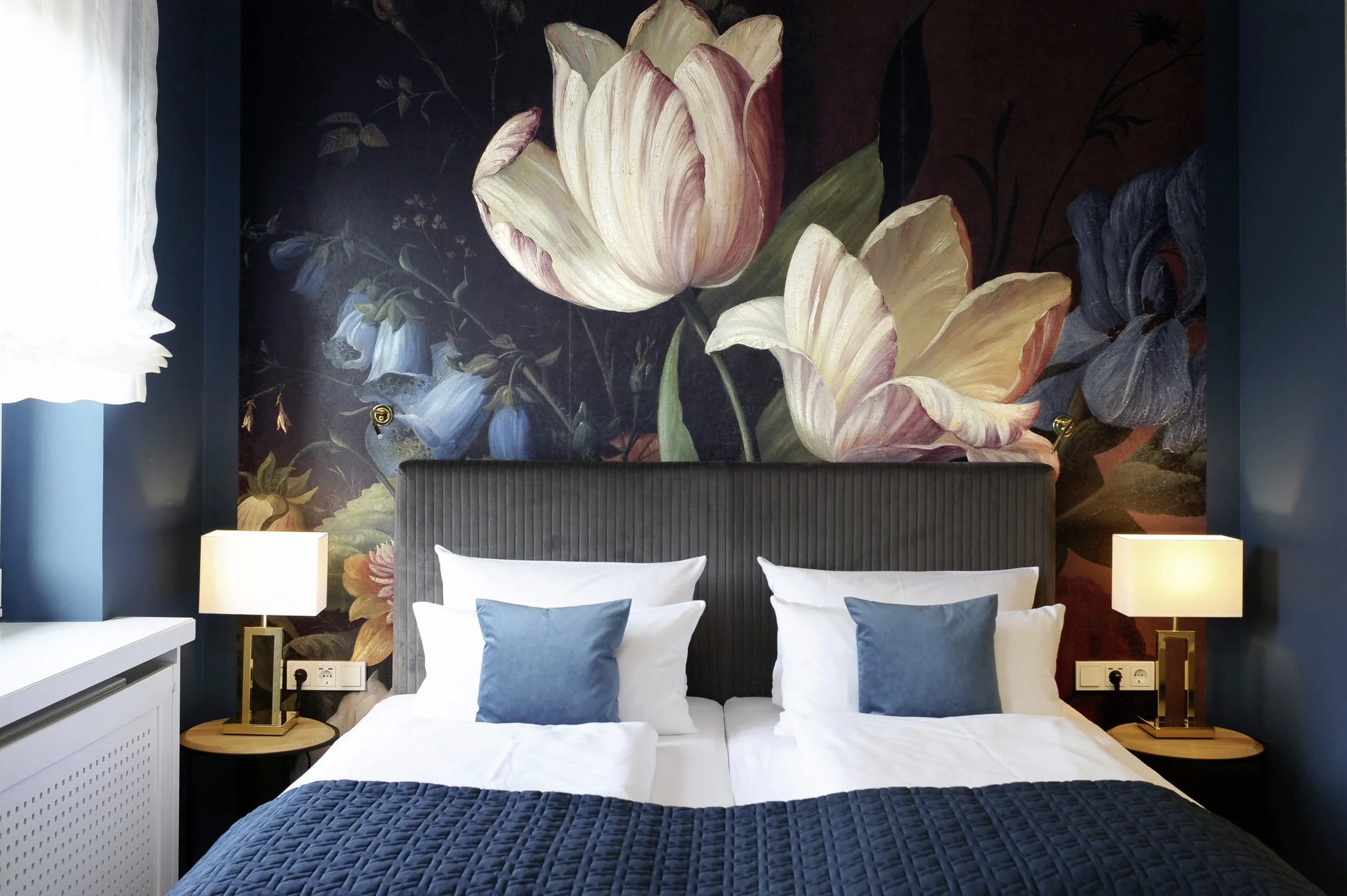 Doppelbett mit dunkelblauem Bettbezug und blauen Kissen vor floralem Wandbild im Michels Wellness- und Wohlfühlhotel