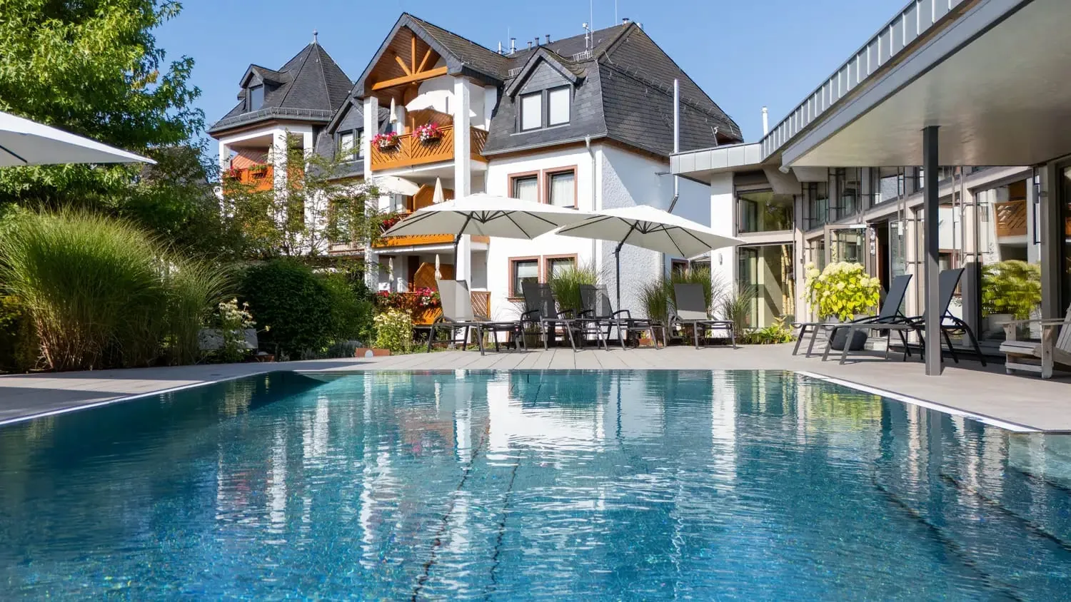 Outdoorpool des Michels Wellness- und Wohlfühlhotels mit Liegestühlen und Sonnenschirmen, umgeben von Garten und Hotelfassade im Hintergrund
