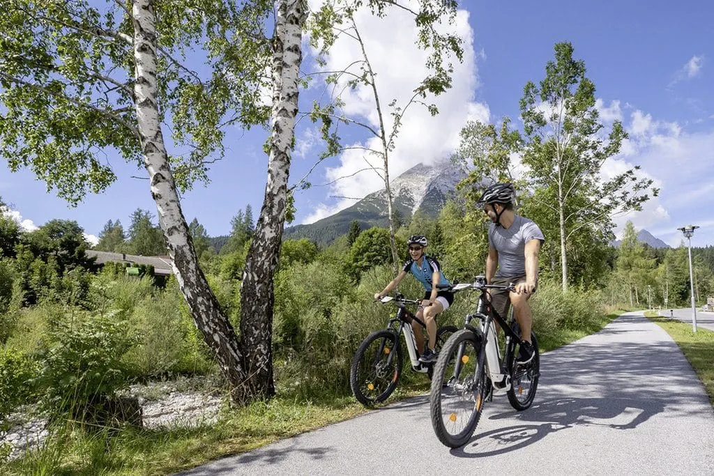 Paar fährt mit E-Bikes auf Radweg neben dem Alpenhotel Karwendel