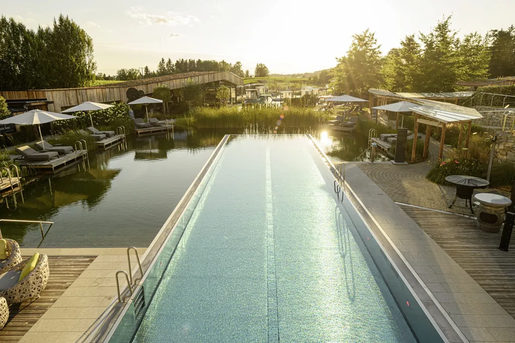 Outdoor-Infinitypool mit Blick auf den Naturteich und Daybeds, umgeben von gr&uuml;ner Landschaft im DAS STEMP bei Sonnenuntergang