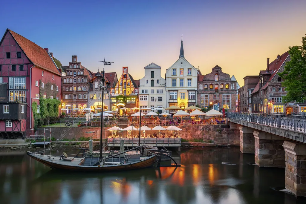 Historische Altstadt von Lüneburg mit beleuchteten Fachwerkhäusern am Abend, Segelschiff im Kanal und Brücke