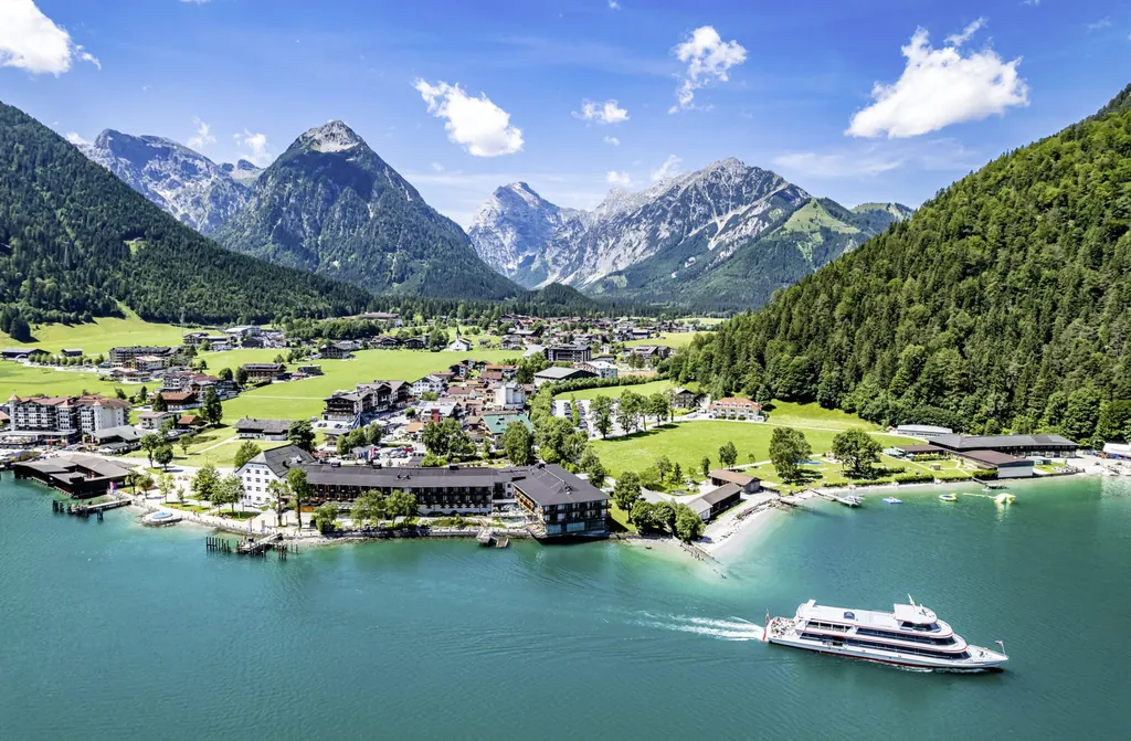 Luftaufnahme vom Achensee mit umgebenden Bergen, grünen Wiesen und Boot auf dem Wasser