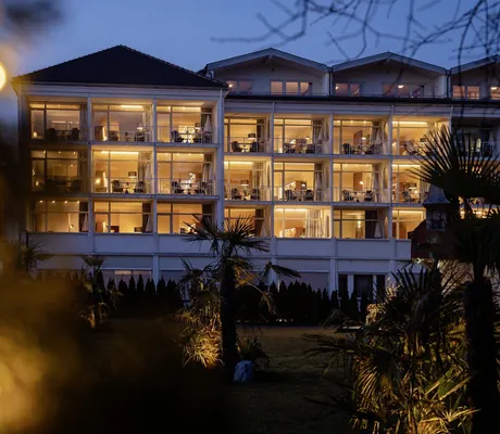 Beleuchtete Fassade des Wellnesshotels Das Parkhotel, umgeben von Palmen und Abendbeleuchtung