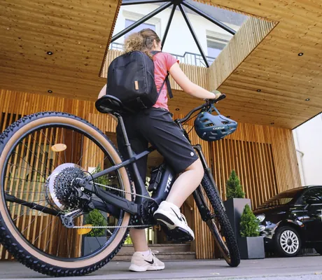 Frau mit Rucksack und Fahrrad vor der stilvollen Eingangshalle mit Holzverkleidung des Wellnesshotels Das Parkhotel