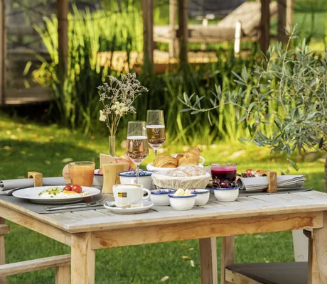 Frühstückstisch im Freien mit Croissants, Obst, Eiern und Getränken, umgeben von grünem Garten und Sonnenschein im Das Parkhotel