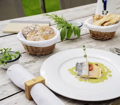 Elegantes Fischgericht mit Kräutersauce, begleitet von knusprigem Brot und frischen Kräutern auf einem Holztisch im Das Parkhotel