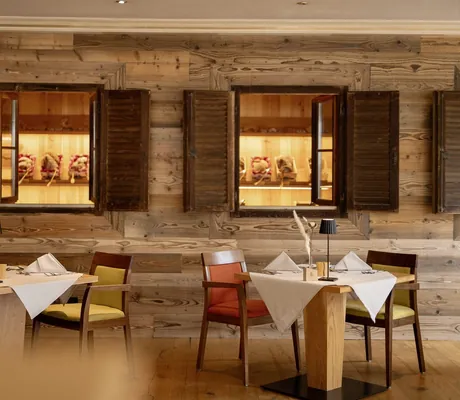 Gemütlich gedeckte Tische mit orange und gelben Stühlen vor einer Wand aus Holz mit Fensterläden und dekorativer Beleuchtung im Restaurant des Das Parkhotel