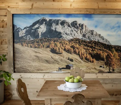 Ländlicher Holztisch mit einer Schale grüner Äpfel, dahinter ein großes Wandbild mit Berglandschaft und Herbstbäumen im Das Parkhotel