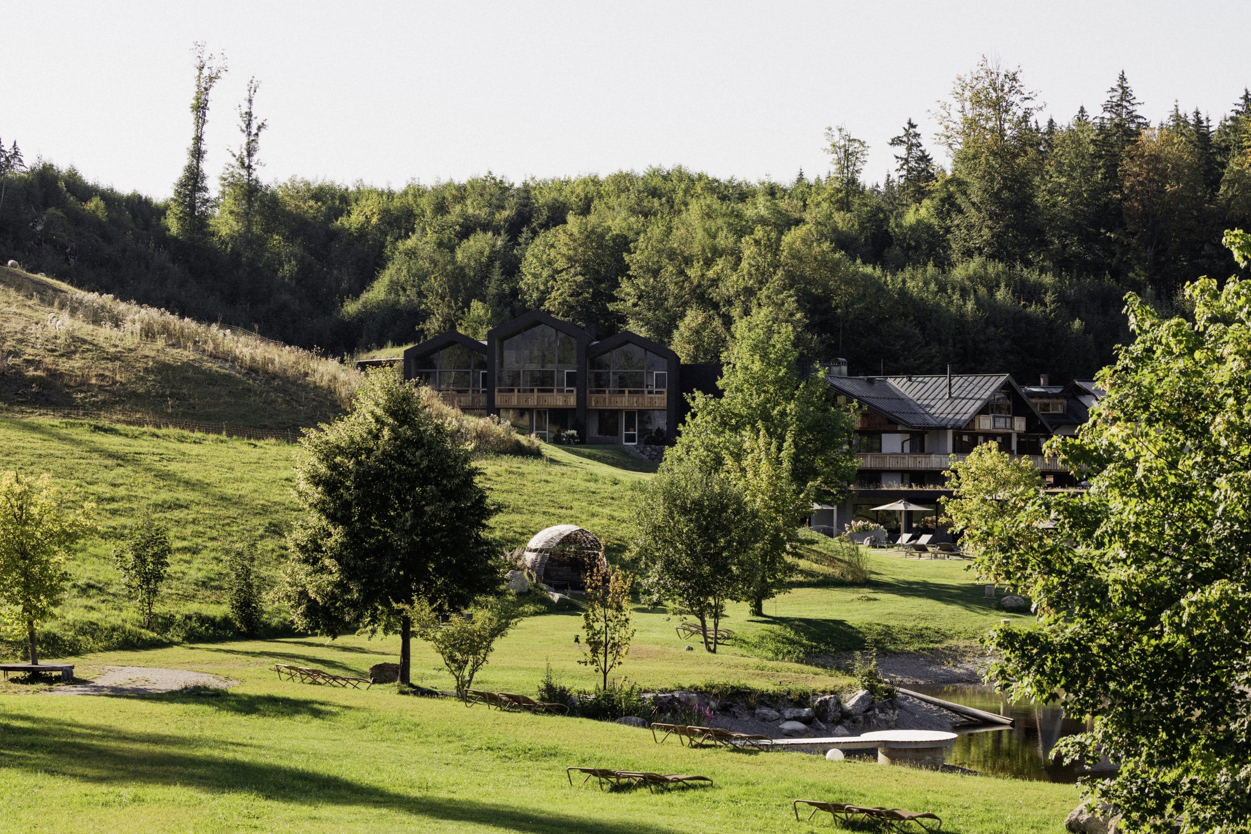 Außenansicht des Berghotel Schlossanger Alp mit neuen Suiten im Hang und Naturteich