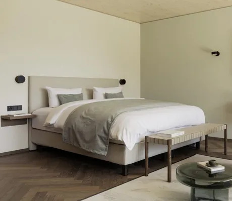 Doppelbett im Schlafzimmer der Suite im Berghotel Schlossanger Alp mit weißem Flauschsessel