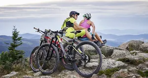 Mountainbiker-Paar sitzt neben den Fahrrädern mit Helmen auf einem Felsen und und schaut in die Landschaft