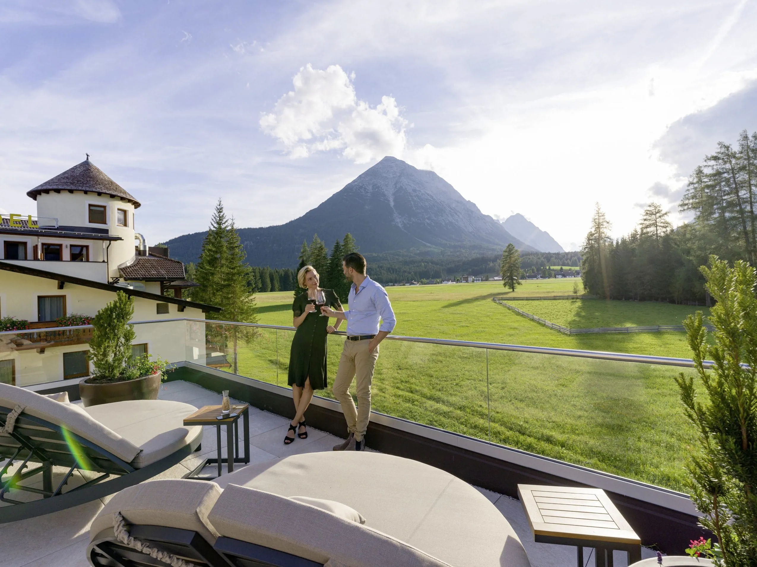 Paar steht auf der Terrasse des Alpenhotel Karwendel und prostet sich mit Blick auf die Berge zu