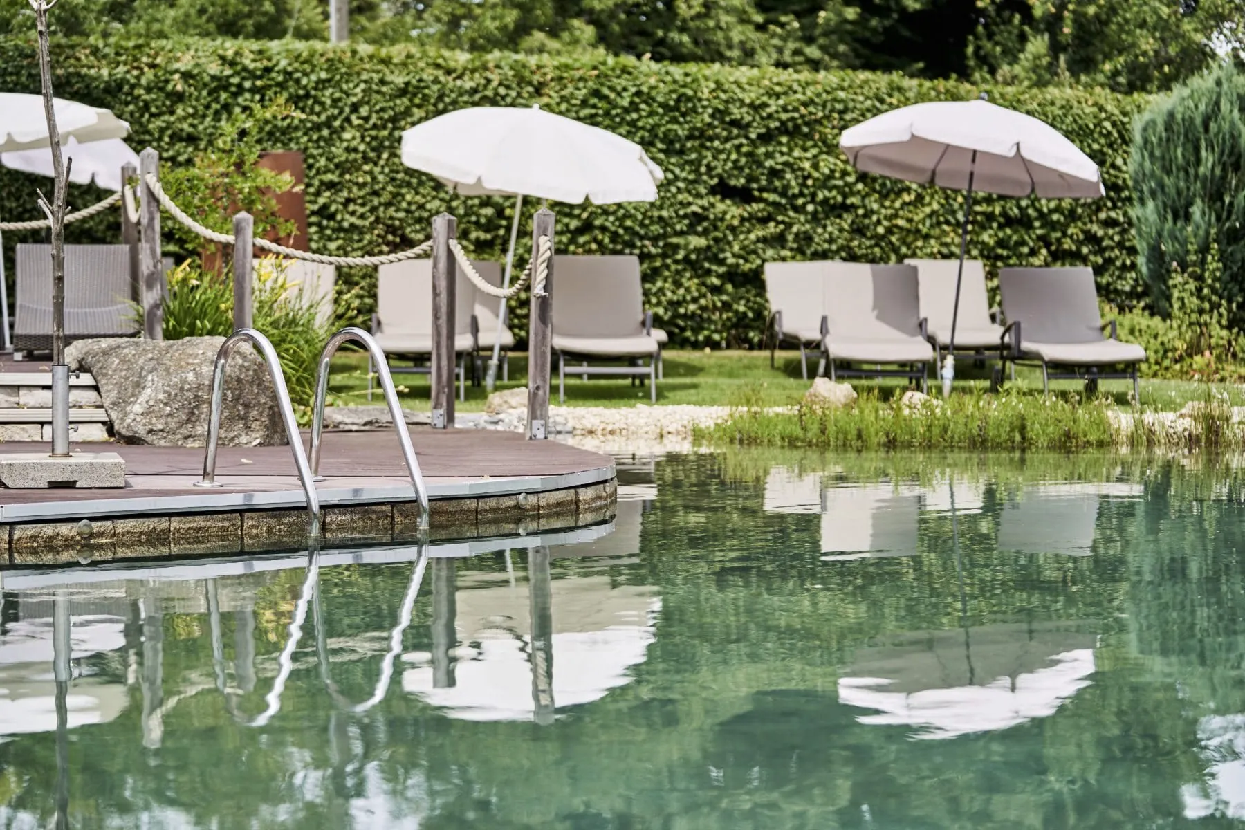 Naturbadeteich des Adults only-Wellnesshotel Zum Br&auml;u mit wei&szlig;en Sonnenschirmen und grauen Liegen