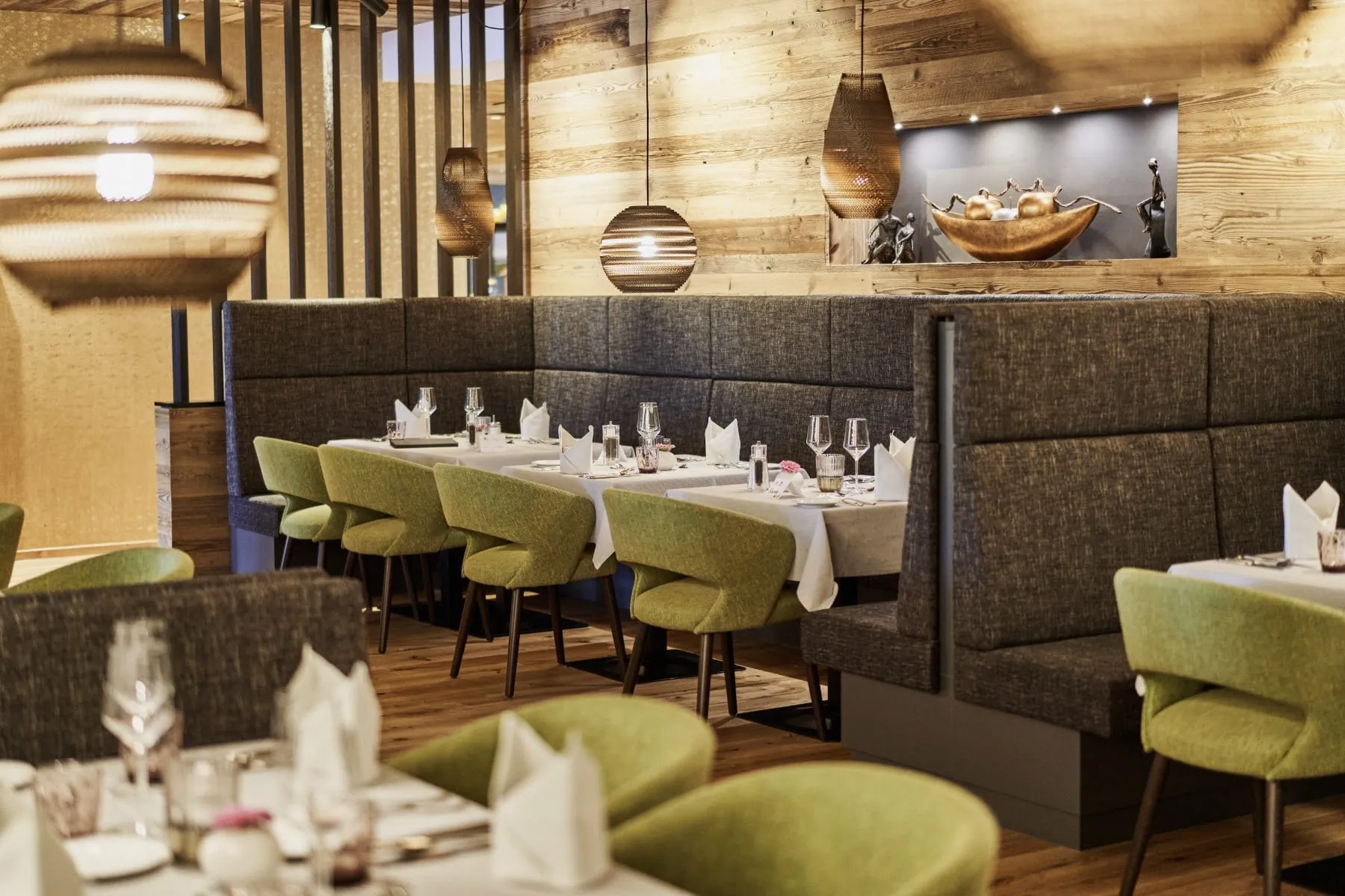 Restaurant im Adults only-Wellnesshotel Zum Br&auml;u mit gr&uuml;nen Polstersesseln und goldener Dekoschale auf einem Regal im Hintergrund