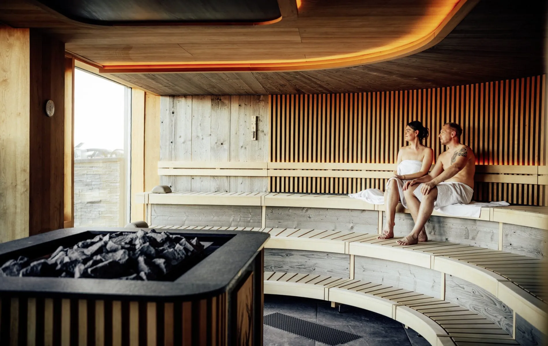 Paar sitzt in der rund geformten Sauna des Adults only-Wellnesshotel Zum Br&auml;u unter roter Deckenleuchte