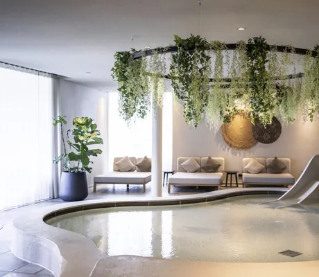 Kinderpool mit geschwungenem Becken, Rutsche und hängender Pflanzen-Dekoration in einem lichtdurchfluteten Raum des Naturresort PURADIES