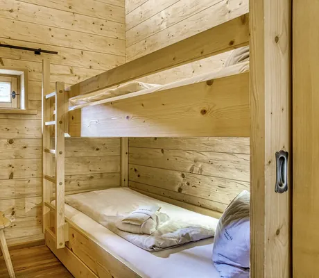 Kinderzimmer mit Etagenbett aus Holz, kleinem Fenster und rustikalem Stuhl mit herzförmiger Aussparung in einem der Chalets des Naturresort PURADIES