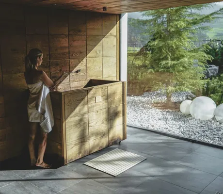 Frau steht in der Sauna des Naturresort PURADIES mit Ausblick auf grüne Landschaft