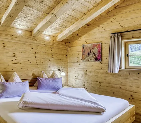 Schlafzimmer in einem der Chalets des Naturresort PURADIES mit Holzverkleidung, gemütlichem Doppelbett und Wandbild