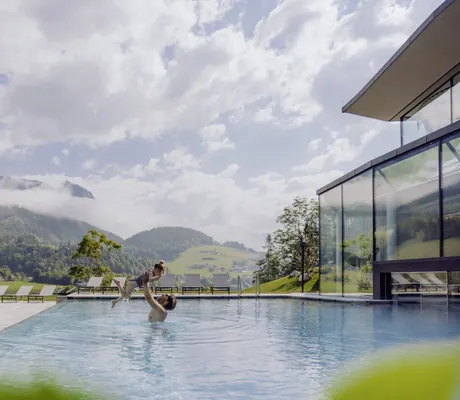 Vater hält Tochter hoch im Outdoor-Infinitypool des Naturresort PURADIES