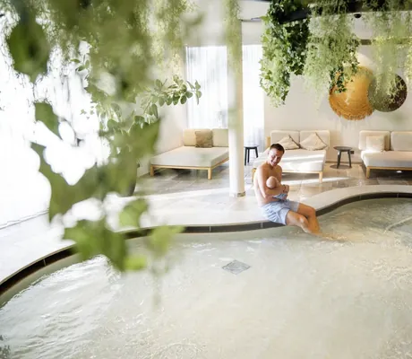 Vater mit Baby am Kinderpool, umgeben von Pflanzen und gemütlichen Sitzmöglichkeiten im Heaven Spa des Naturresort PURADIES