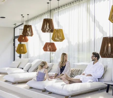 Familie entspannt auf Liegen im modernen Ruheraum mit großen Fenstern und dekorativen Lampen im Naturresort PURADIES