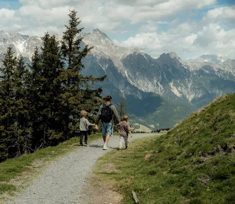 Vater mit zwei Kindern auf einem Wanderweg in den Bergen mit Blick auf die grünen Täler und steilen Gipfel in der Nähe des Naturresort PURADIES