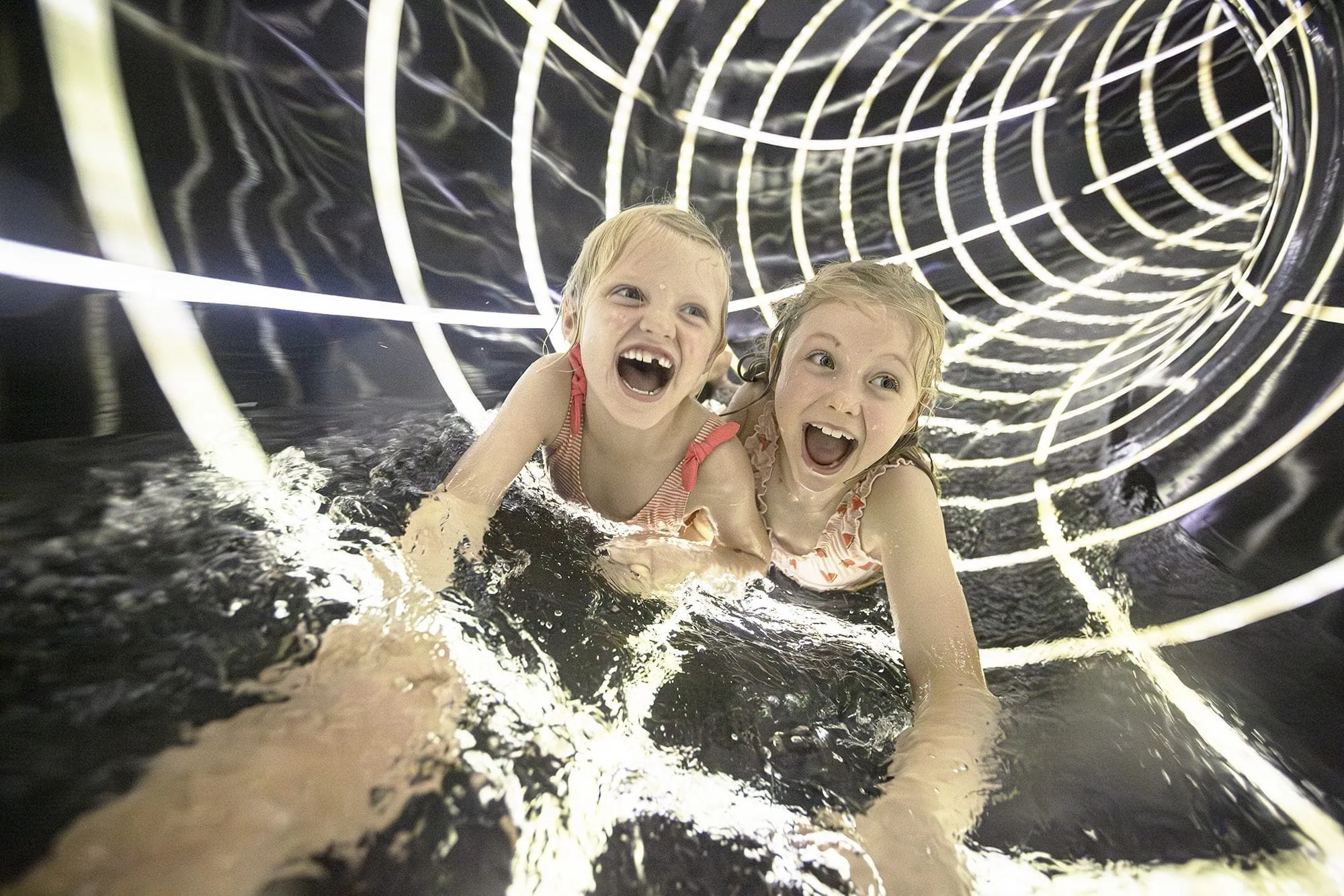 Zwei Mädchen in Badesachen in einer Rutsche des Familotel Allgäuer Berghof mit spiralförmigen Lichtern