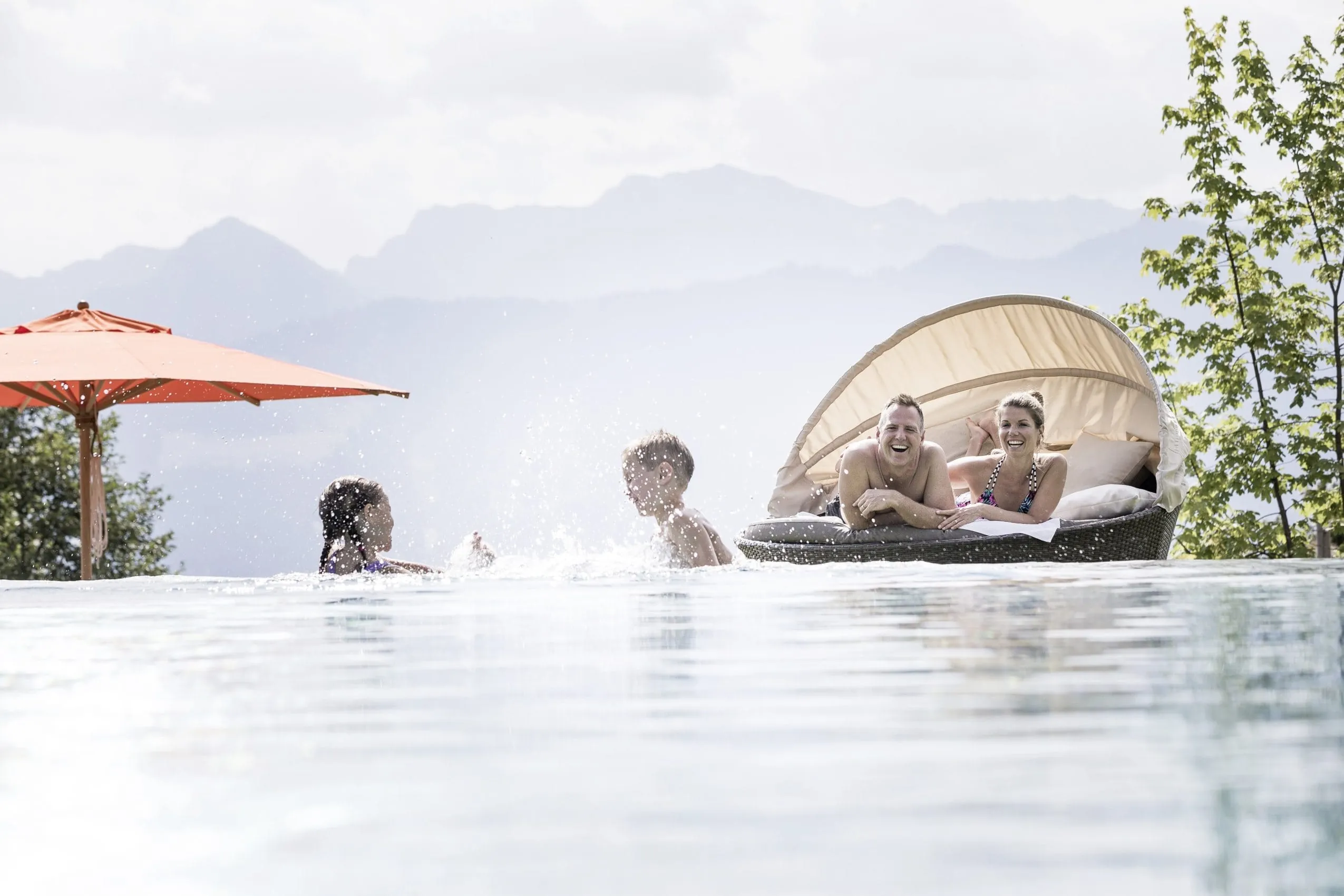 Pärchen liegt im Ruhenest, während die Kinder im Outdoorpool des Familotel Allgäuer Berghof plantschen