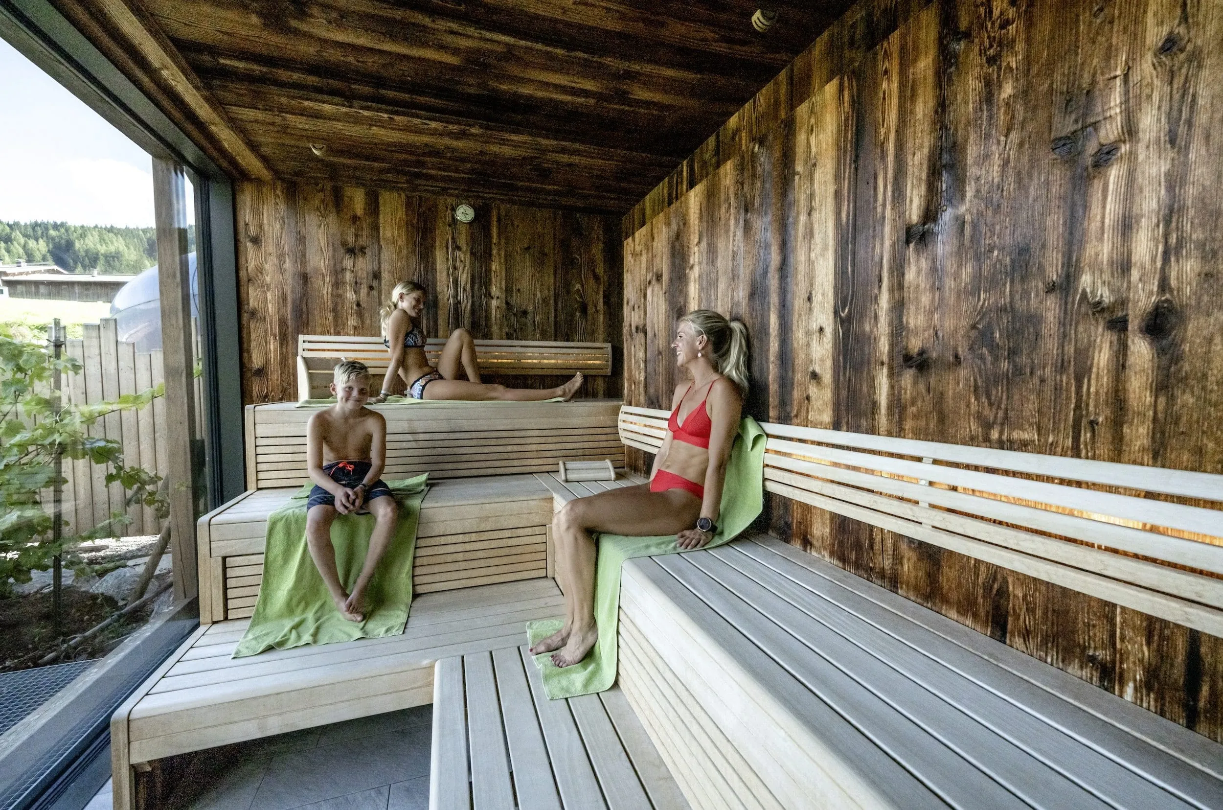 Blonde Frau sitzt mit zwei Jugendlichen in der Sauna des Good Life Resorts Riederalm