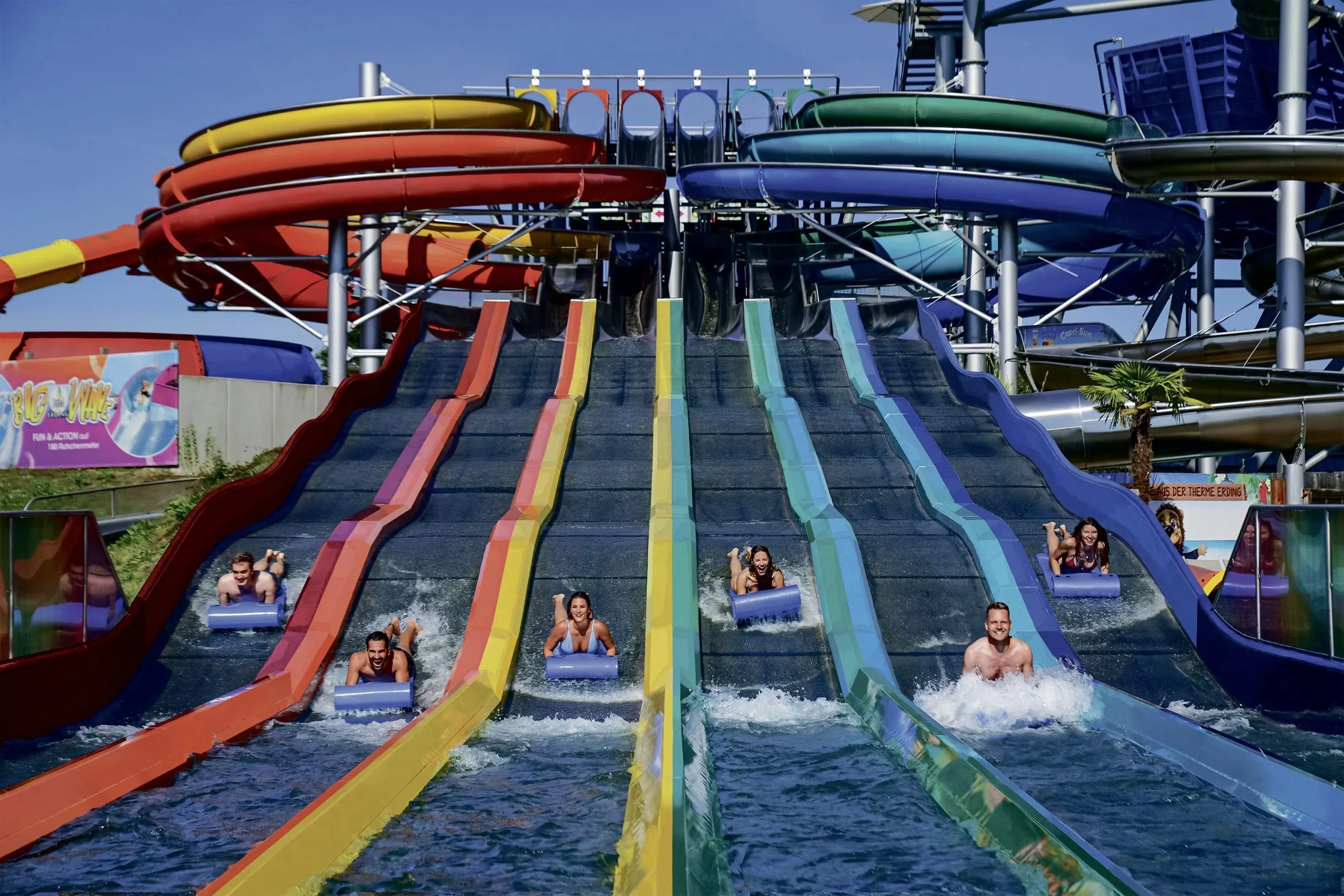 Sechs Personen rutschen die bunte Rainbow Wasserrutsche auf einer Matte herunter im Hotel Victory Therme Erding