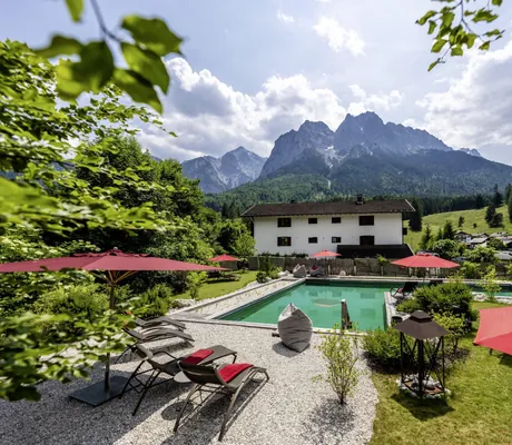 türkiser Naturpool im Bayern Resort mit Sonnenliegen und roten Sonnenschirmen mit Blick auf die Berge