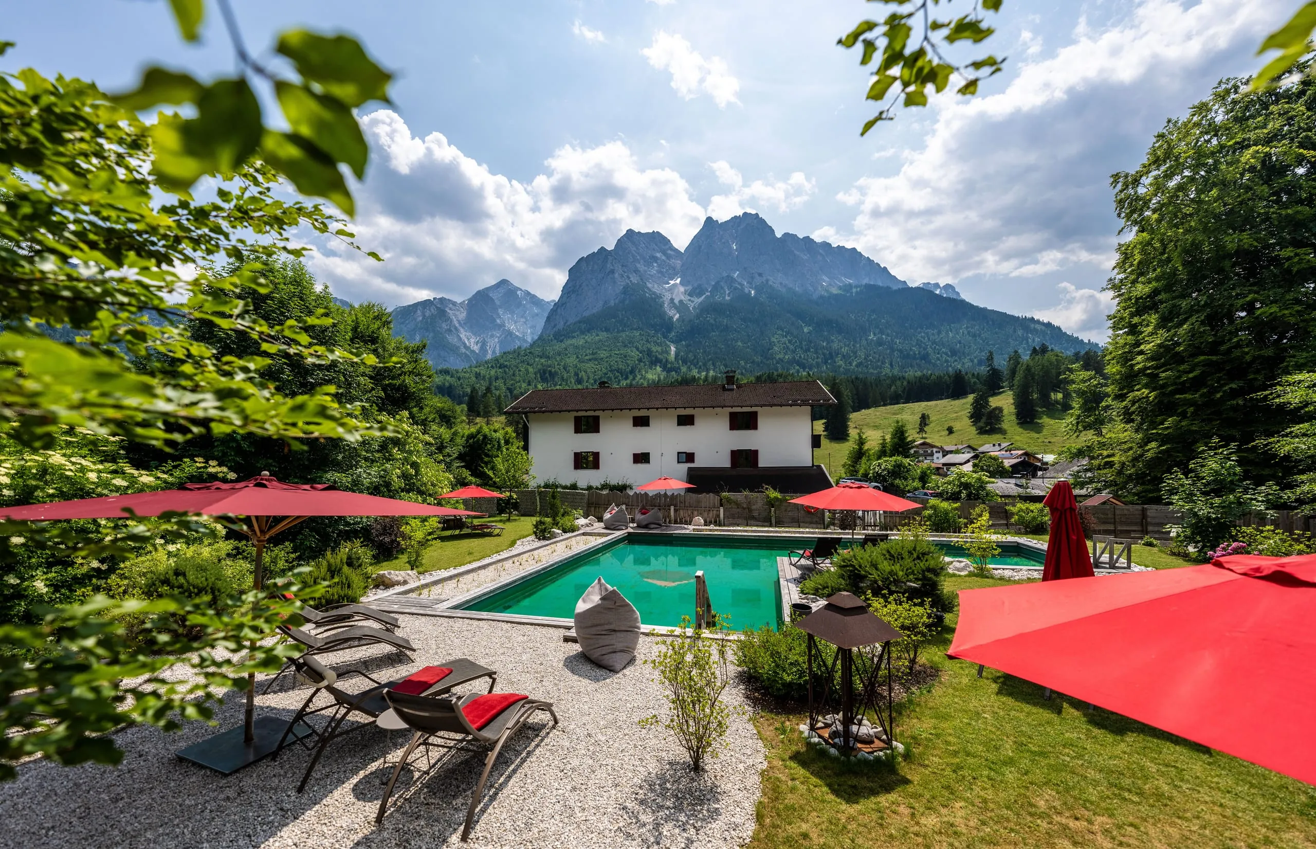 Outdoorpool im Bayern Resort mit Liegen, roten Sonnenschirmen und Panoramablick auf die Zugspitze.