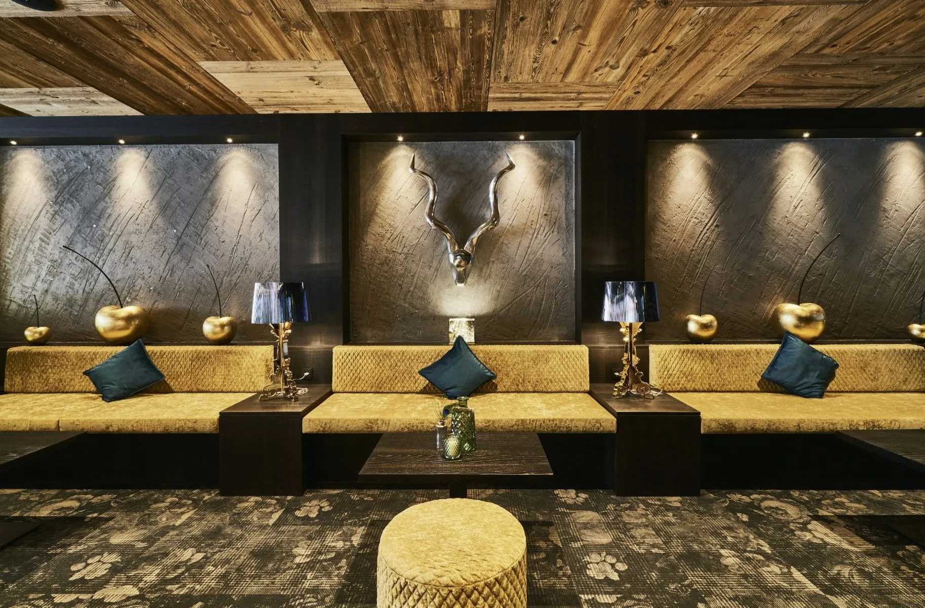 goldene Polsterb&auml;nke in der Lobby des Wellnesshotel Zum Br&auml;u mit silbernem Hischgeweih und goldenen Deko&auml;pfeln